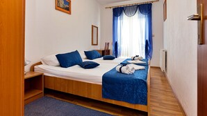 A hotel room with a wooden bed, blue bedding, a small bedside table, a nightstand, a window with blue curtains, and a picture on the wall. - Villa Saba by Interhome (Trogir)