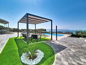 Área de piscina no terraço com pergolado, assentos e vista para o mar.