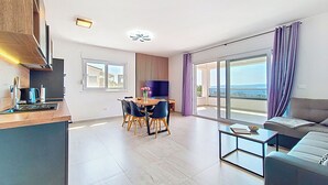 A modern apartment with a dining area, a sofa, a TV, and a balcony with a view.