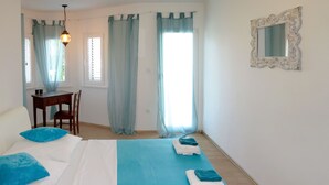 A bedroom with a bed, a desk, and a chair. There are curtains on the windows, and a mirror on the wall.