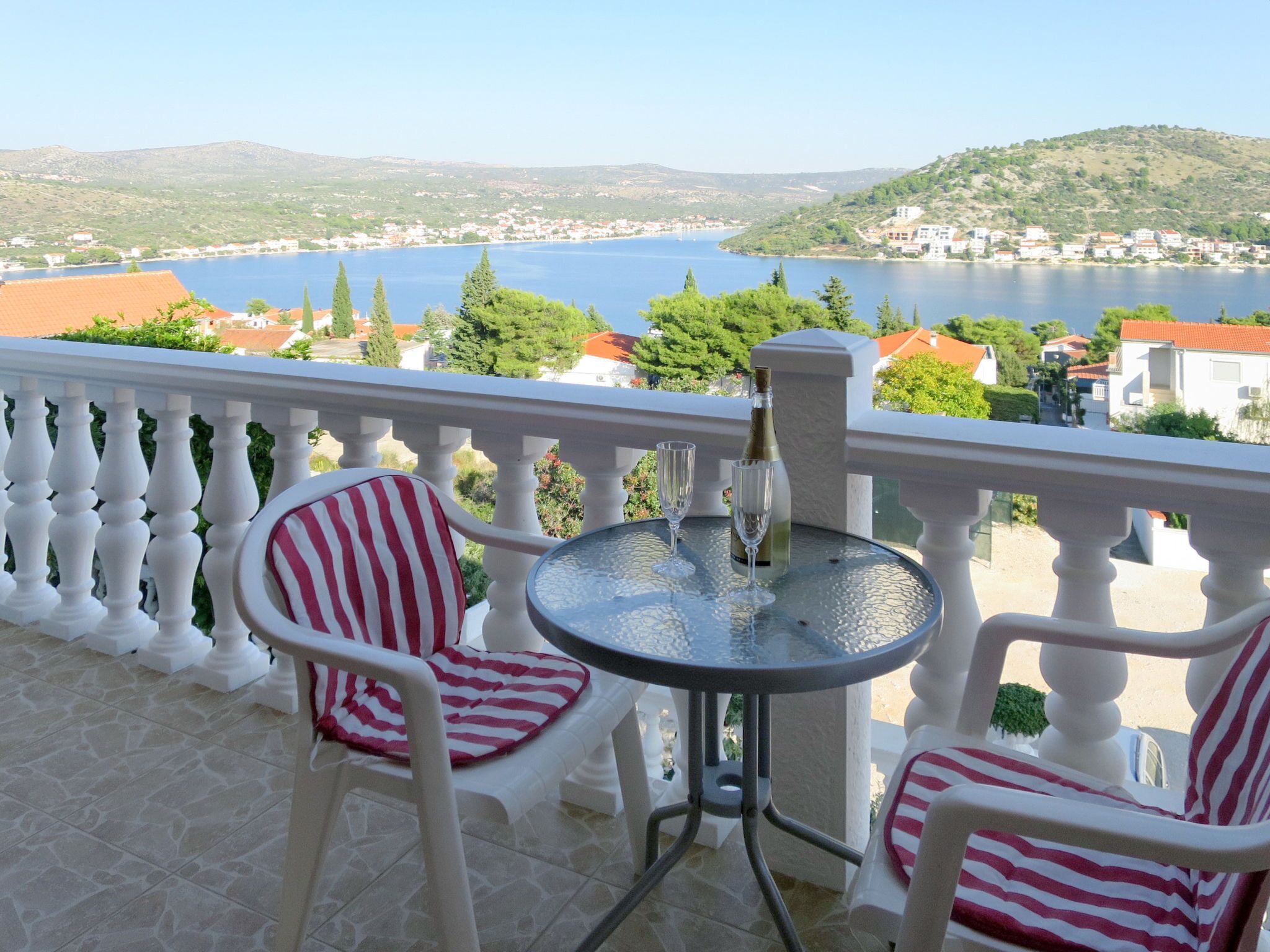 A balcony with two striped chairs and a small round table, overlooking a lake and a town.