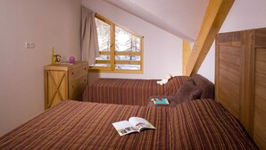 A small, cozy room with two beds, a wooden dresser, and a window with a view of trees. - Parc des Airelles by Interhome (Les Orres)