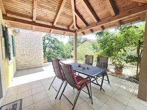 Un patio couvert avec une table et des chaises, un mur en pierre et une vue sur la verdure.