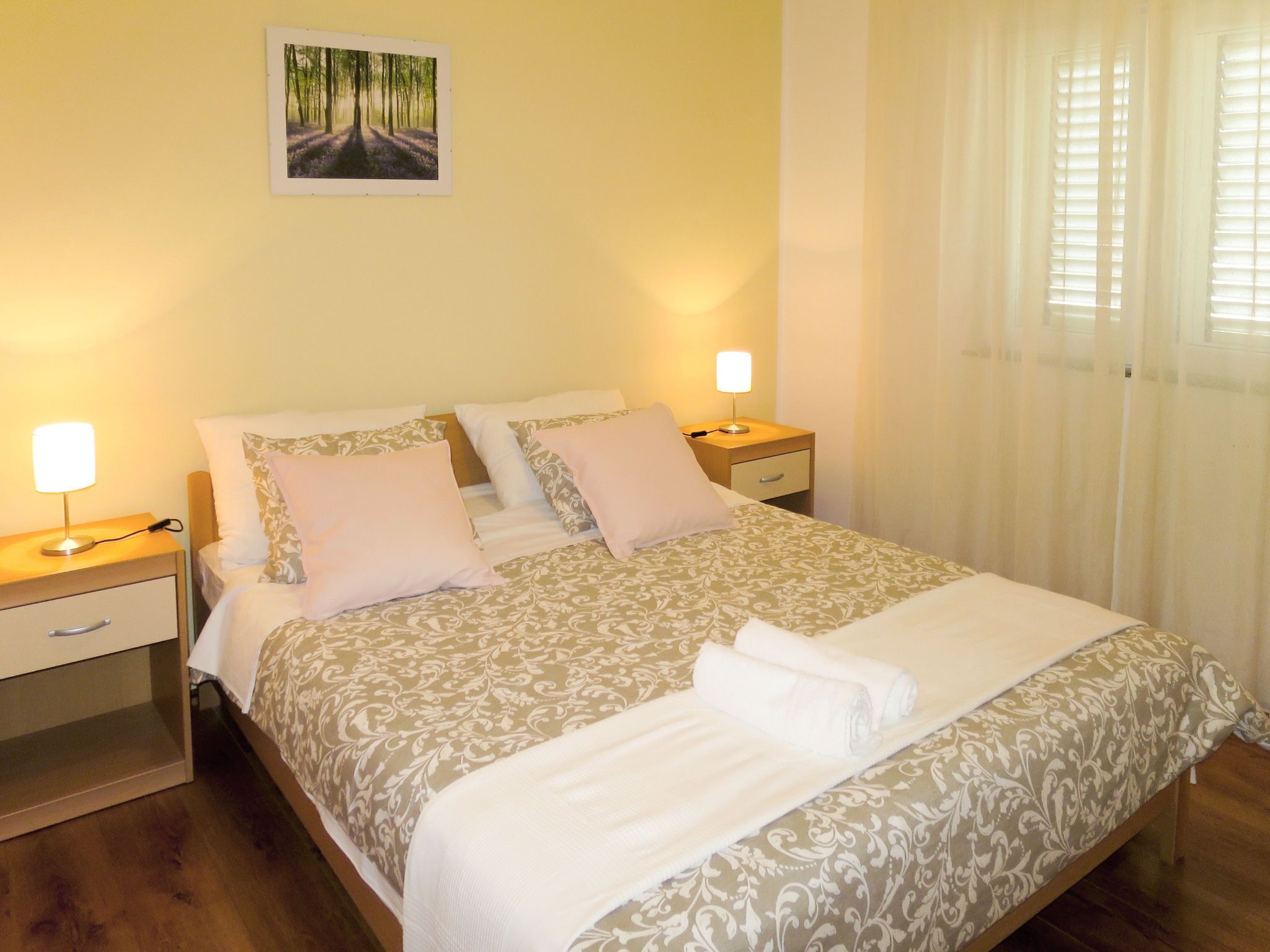 A neatly made bed with a patterned bedspread, two bedside tables with lamps, and a framed picture on the wall.