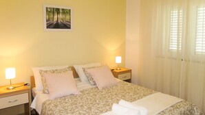 A neatly made bed with a patterned bedspread, two bedside tables with lamps, and a framed picture on the wall. - Apartment Toni by Interhome (Šibenik)