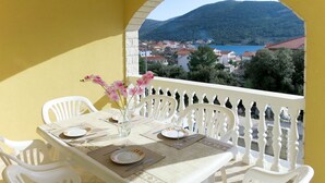 A table set for two with white chairs, a vase with flowers, and a view of a town and mountains in the background. - Apartment Toni by Interhome (Šibenik)
