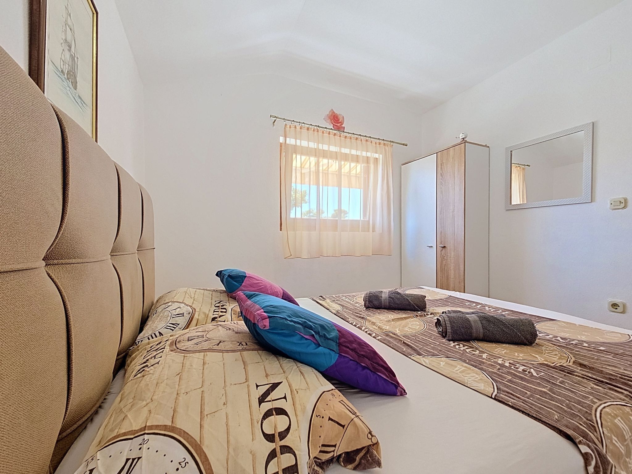 A bedroom with a bed, a window with curtains, a wardrobe, and a mirror.