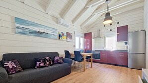 Un interior moderno con piso de madera, un sofá con cojines florales, una mesa de comedor con sillas, una zona de cocina con refrigerador y obras de arte en las paredes.