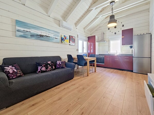 A modern interior with a wooden floor, a sofa with floral cushions, a dining table with chairs, a kitchen area with a refrigerator, and artwork on the walls. - Vacation home Dada by Interhome (Biograd na Moru)