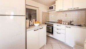 A compact kitchen with white cabinets, a microwave, a toaster, and a bowl of fruit on the counter. - Apartment Ana by Interhome (Biograd na Moru)