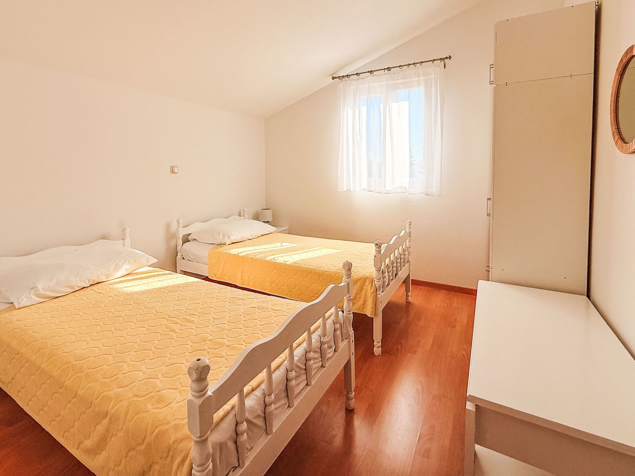 Un dormitorio con dos camas, una ventana con cortinas translúcidas y un armario de madera.