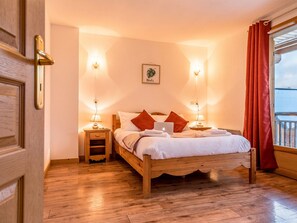 A wooden bed with white and red bedding, two bedside tables with lamps, a framed picture on the wall, and a window with red curtains.