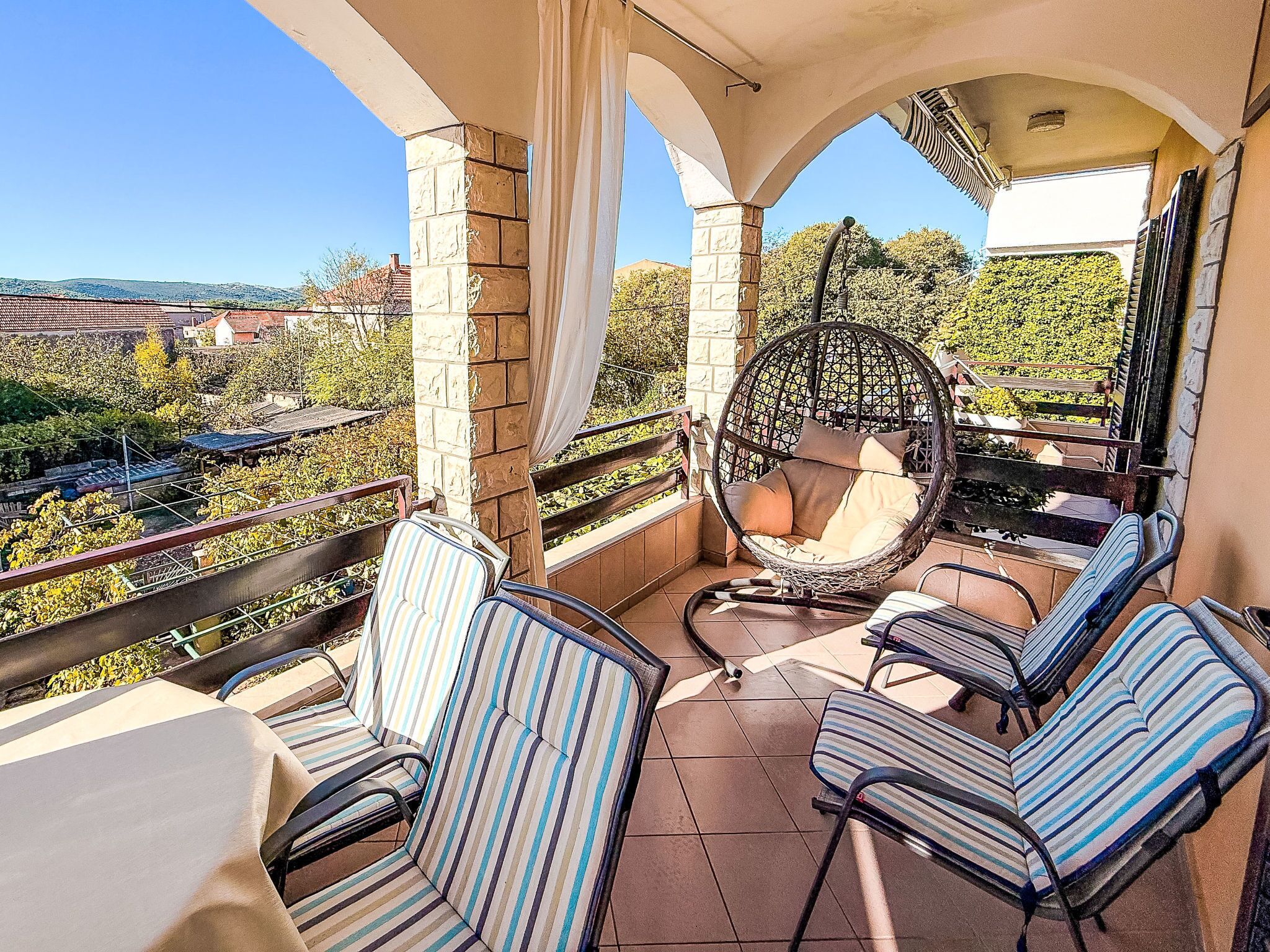 A balcony with a hanging chair, striped chairs, and a view of the surrounding area.
