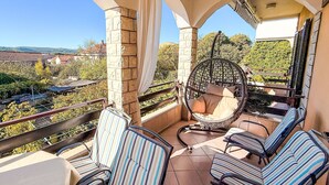 A balcony with a hanging chair, striped chairs, and a view of the surrounding area. - Apartment Ana by Interhome (Biograd na Moru)