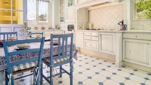 A kitchen with white cabinets, a dining table with blue chairs, and a window with curtains. - Vacation home Solena by Interhome (Flayosc)