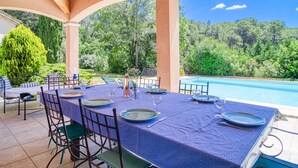 An outdoor dining area with a table set for four, surrounded by chairs, overlooking a swimming pool and lush greenery. - Vacation home Solena by Interhome (Flayosc)