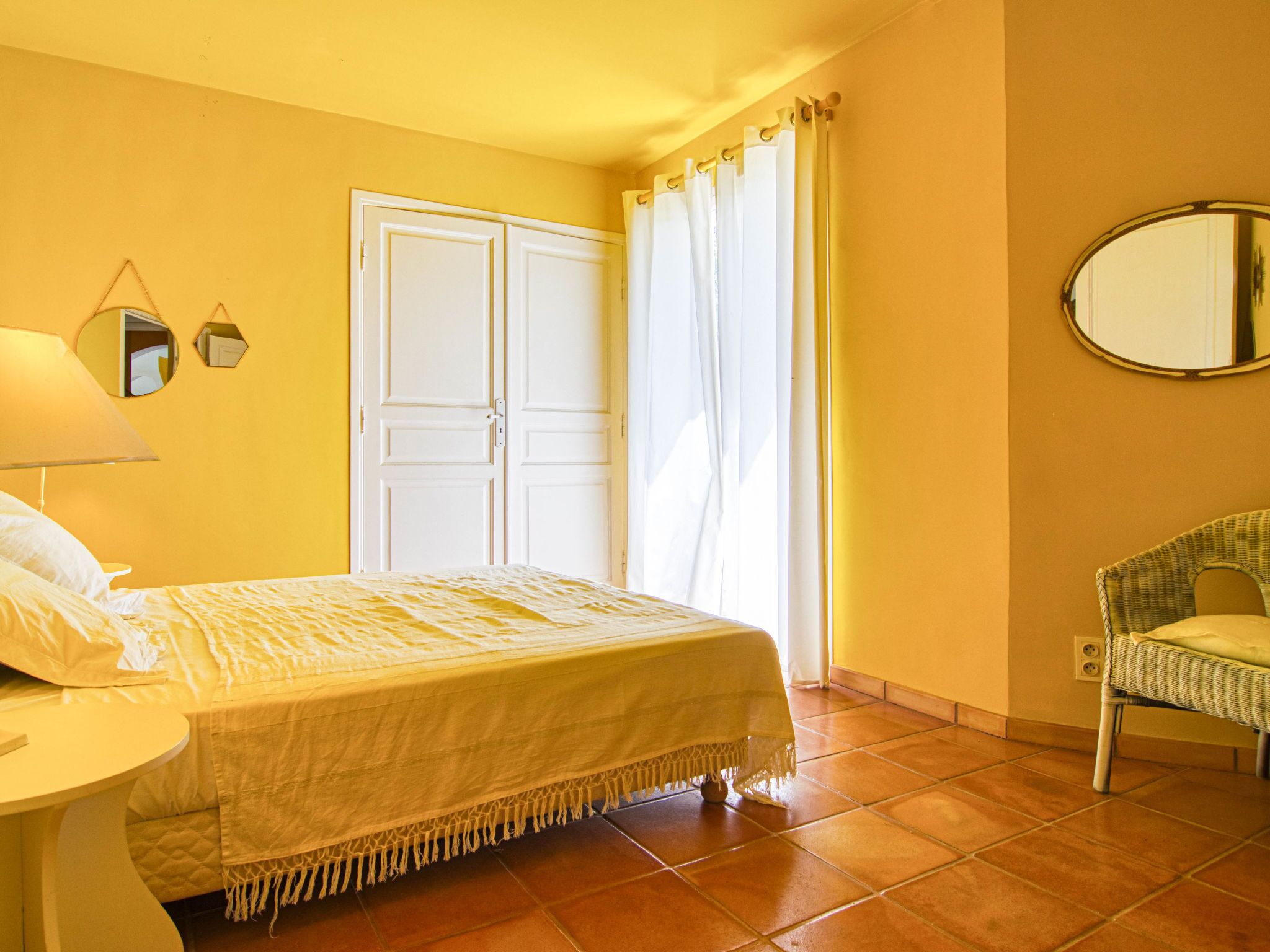 A room with a bed, a chair, a mirror, and a door.
