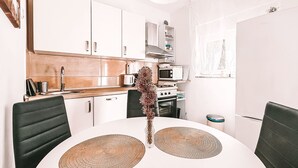 A modern kitchen with white cabinets, a microwave, a kettle, and a dining table with two chairs.