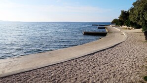 A coastal walkway with a pebble beach, a concrete path, and a clear view of the sea.