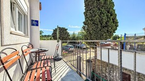 A balcony with wooden chairs and a table, a sign reading "ARBEITEMAN", and a view of parked cars and a tall tree.