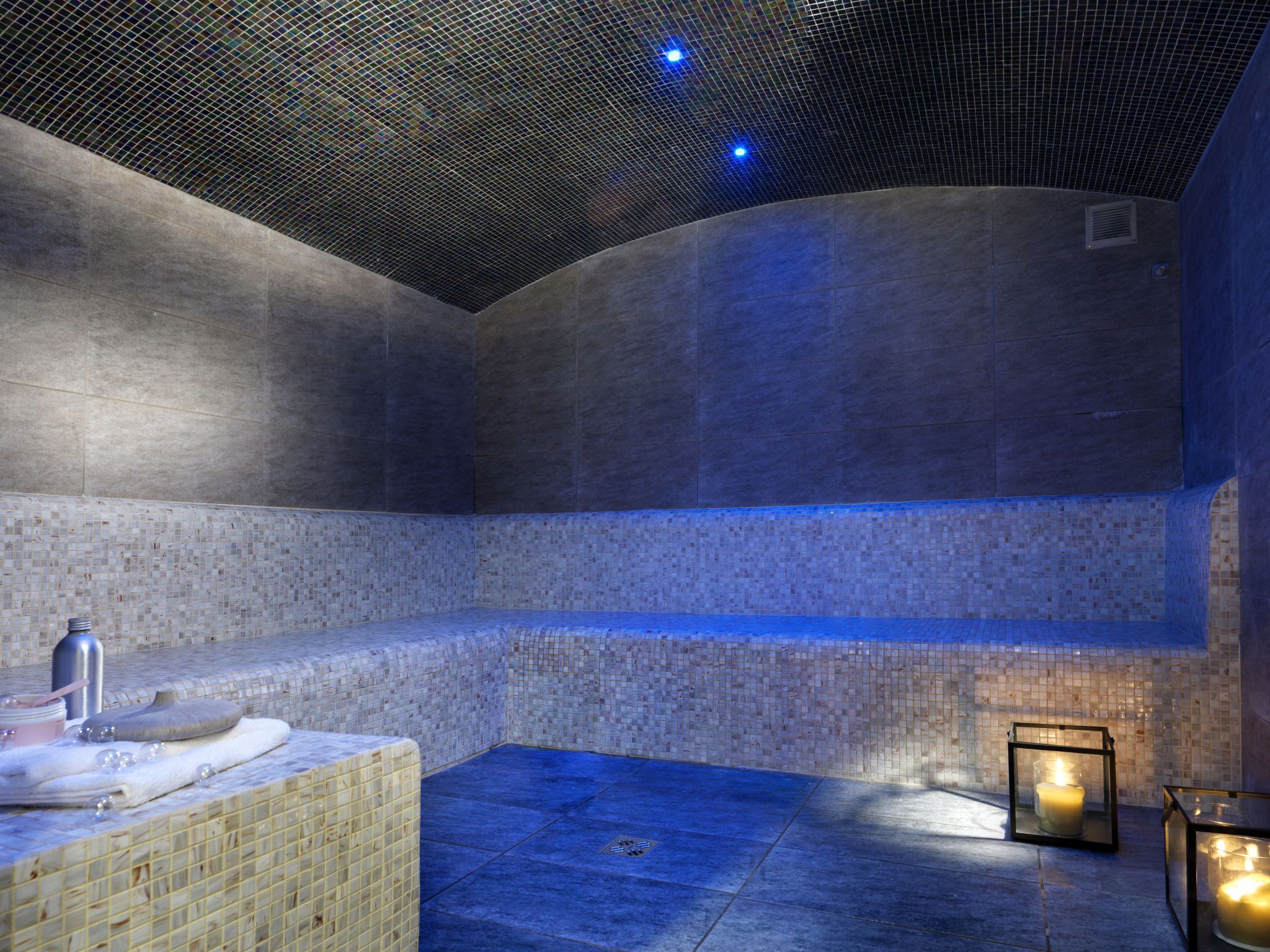 A modern spa room with a tiled floor, a bench, a sink, and candles.