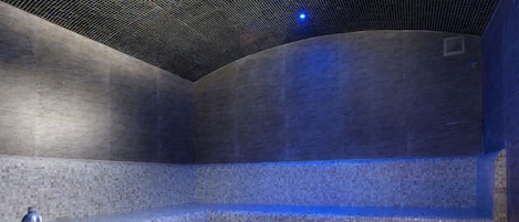 A modern spa room with a tiled floor, a bench, a sink, and candles.