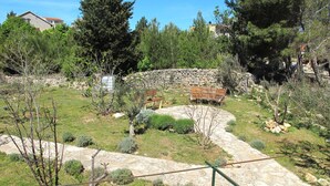 Un chemin de pierres mène à un banc situé dans un jardin aménagé, agrémenté d’arbres et bordé d’un mur de pierres.