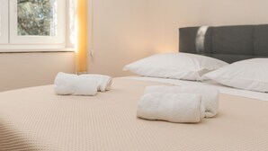 Un lit bien fait, avec des oreillers et des serviettes blancs, une fenêtre donnant sur des arbres et un tableau représentant un coucher de soleil accroché au mur.