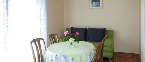 A dining area with a round table, chairs, a vase of flowers, a green sofa, and a ceiling fan.