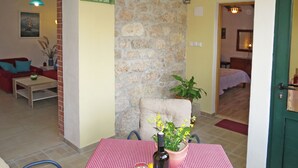A dining area with a red and white checkered tablecloth, a bottle of wine, and a glass. There is a stone wall and a door leading to another room.