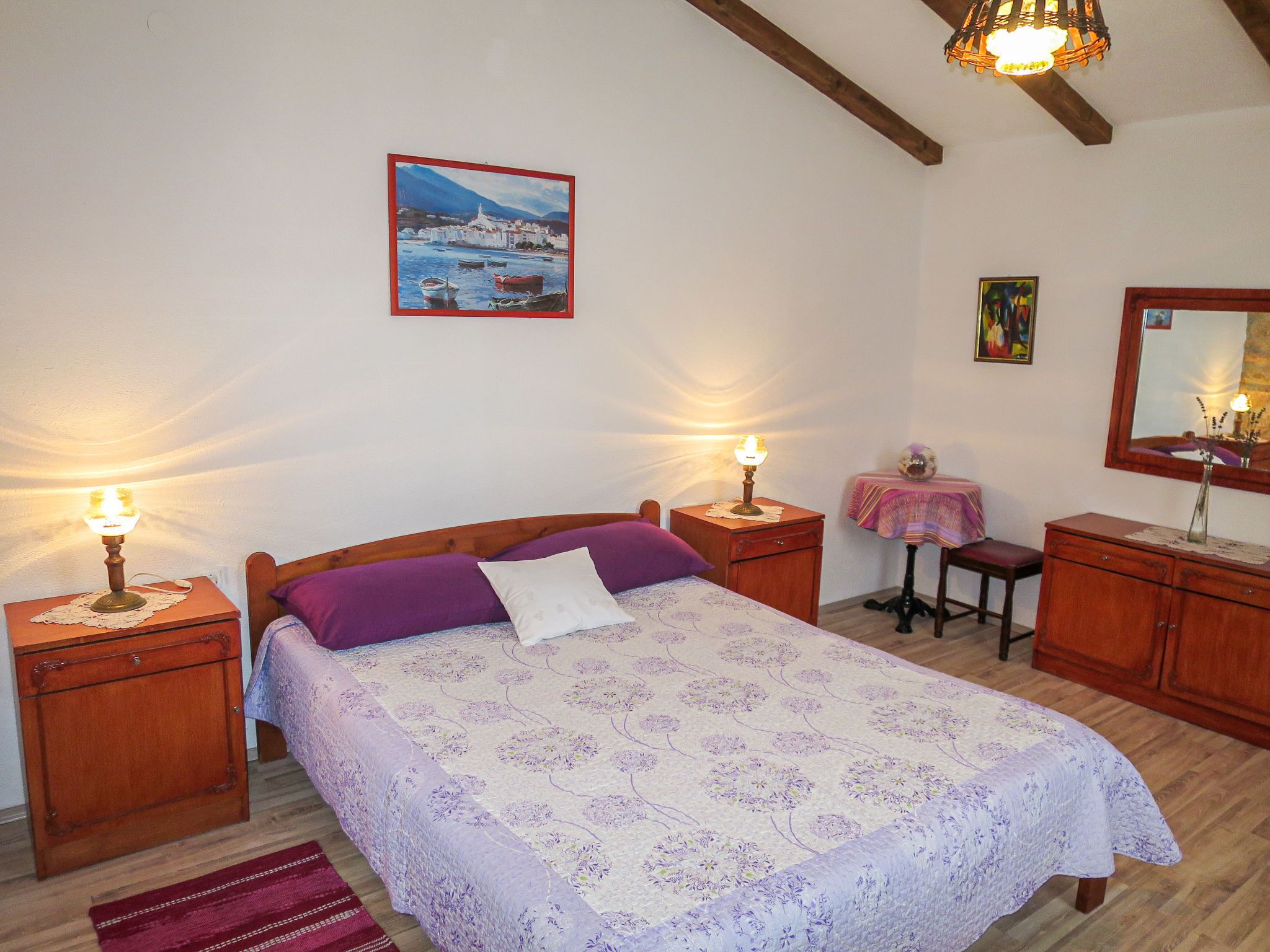 A bedroom with a bed, bedside tables, a nightstand, a dresser, a mirror, a painting on the wall, and a lamp.