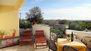 A terrace with wooden chairs and a table, potted plants, and a view of the landscape.