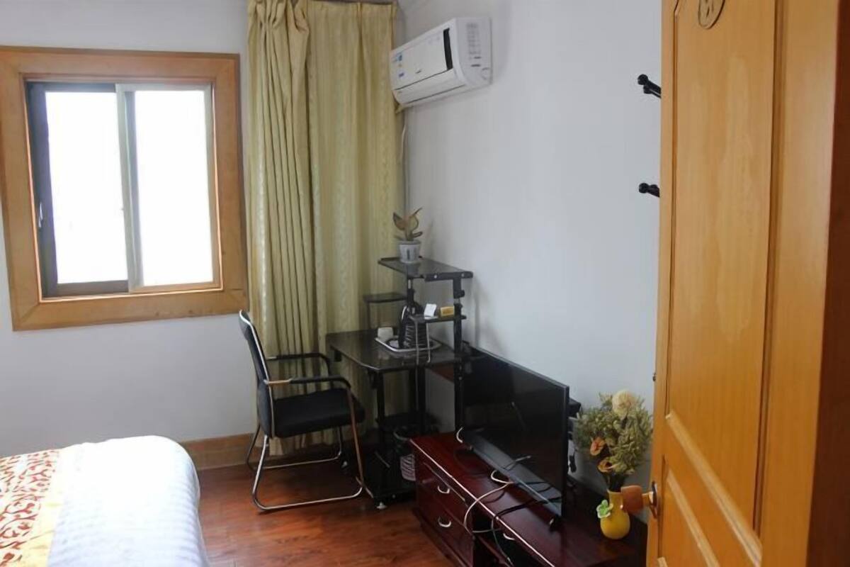 A bedroom with a bed, a desk with a chair, a potted plant, and a wooden door.