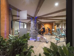 A gym with exercise equipment, a stone pillar, wooden beams, and indoor plants.