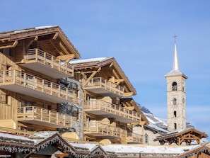 A wooden chalet with balconies, a stone bell tower, and a snowy mountain backdrop. - Kalinda Village 5* by Interhome (Tignes)
