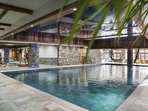 An indoor swimming pool with stone walls and wooden beams, surrounded by lounge chairs and a view of the sky. - Kalinda Village 5* by Interhome (Tignes)