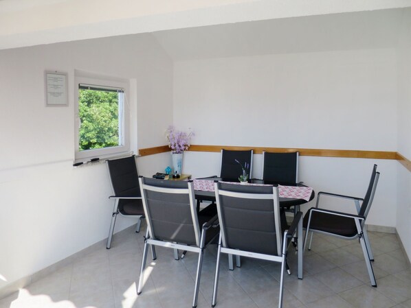 A dining area with a table and four chairs, a window with a view of trees, and a small vase with flowers on the table.