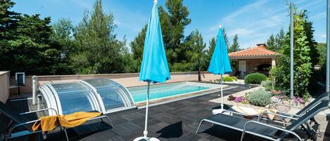 Ein Poolbereich mit Liegestühlen, einem Pool mit Glasveranda und einem Gebäude mit Ziegeldach im Hintergrund.