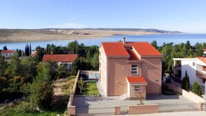 Un bâtiment moderne avec un toit recouvert de tuiles rouges, entouré de verdure et avec une étendue d’eau en arrière-plan.