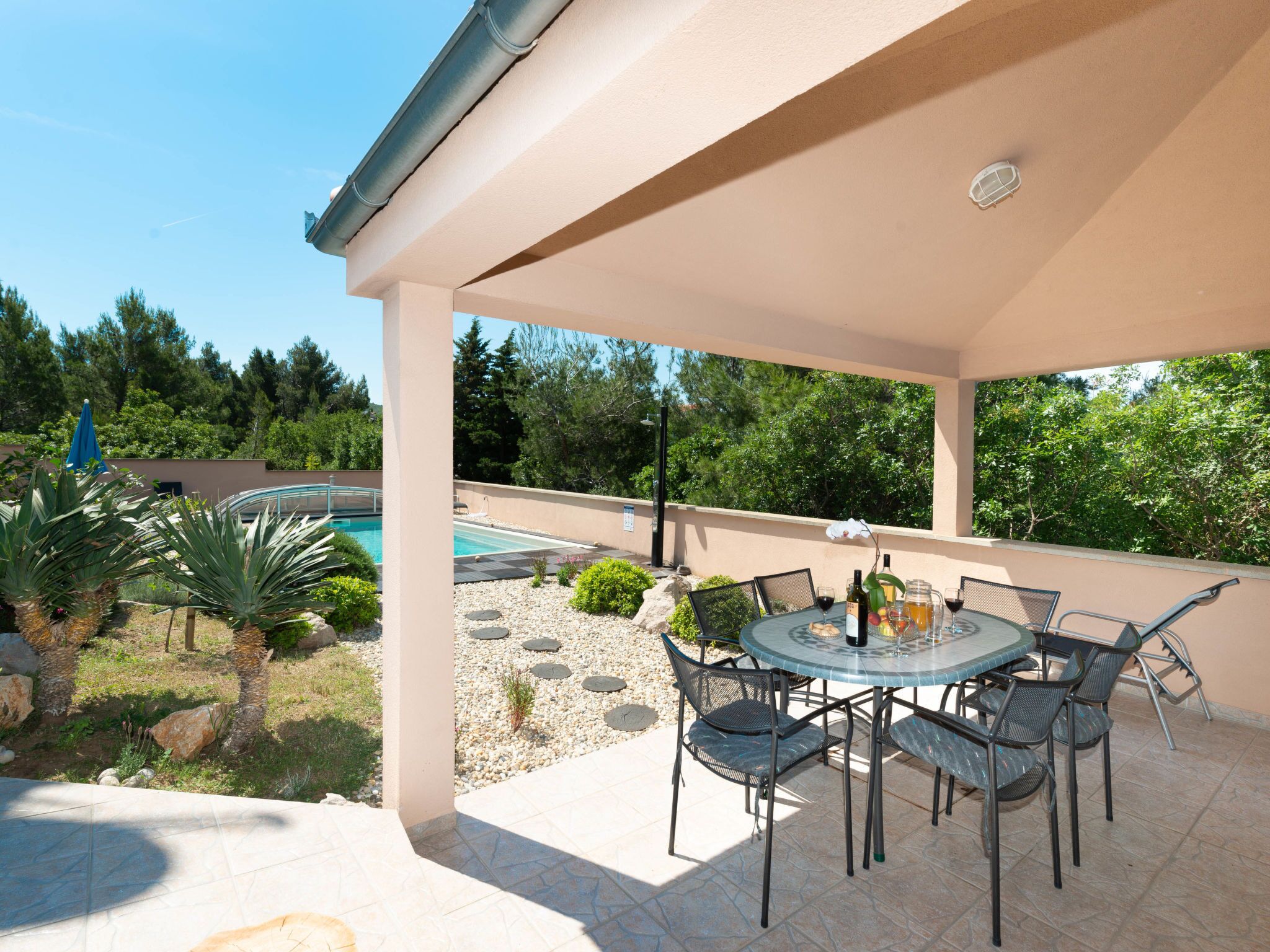 Un patio couvert avec une piscine, des sièges d’extérieur et une vue sur l’espace piscine.