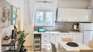 A modern kitchen with white cabinets, a dining table with chairs, a window with curtains, and a small refrigerator. - Katarina by Interhome (Starigrad-Paklenica)