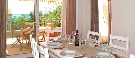 A dining area with a table set for four, a bottle of wine, and a view of the outdoors.