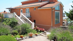 A two-story house with a red-tiled roof, a balcony with white balustrades, and a garden with various plants and flowers. - Valentina by Interhome (Novi Vinodolski)