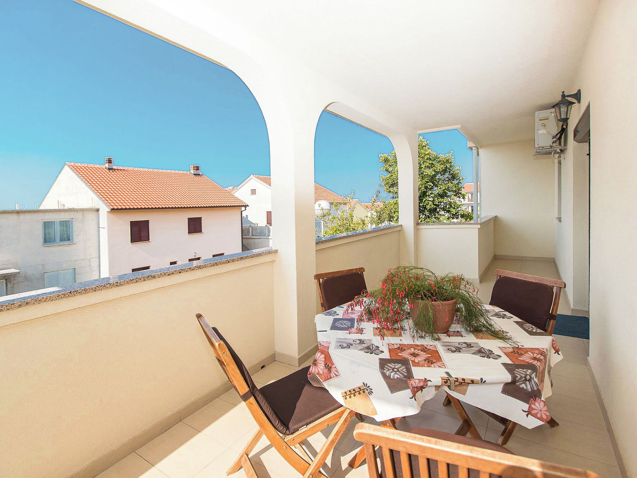 Ein Balkon mit Tisch für zwei Personen, Stühlen, einem Blumentopf und Blick auf angrenzende Gebäude.