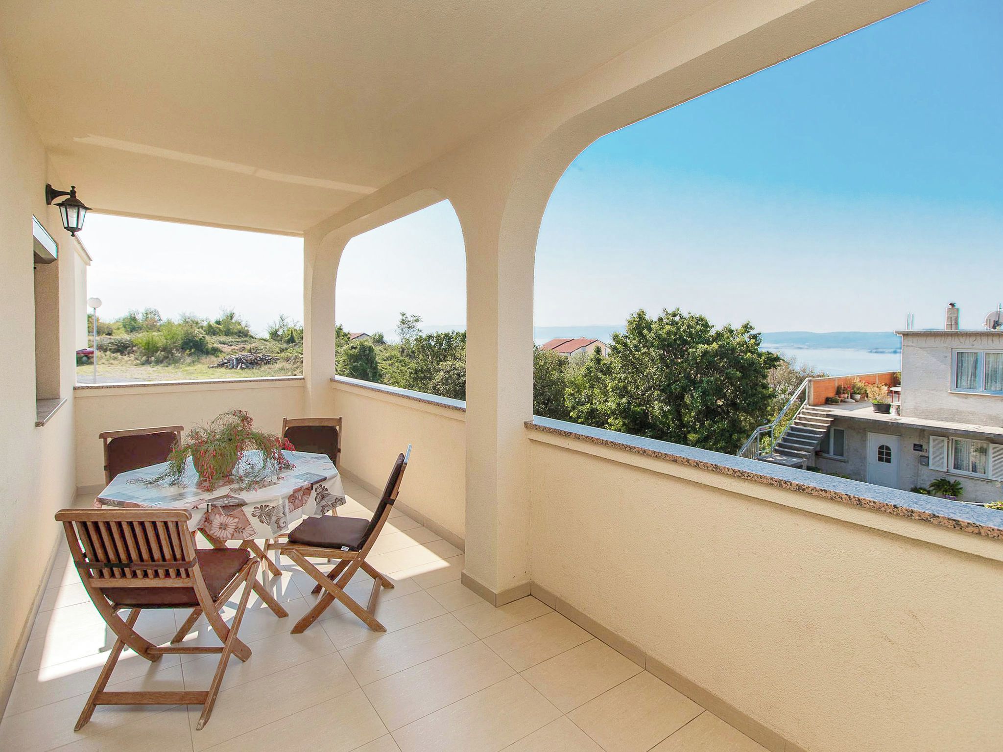 Un balcon avec une table et des chaises, une vue sur la mer et un ciel dégagé.