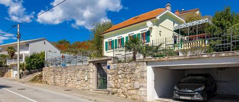A two-story house with a stone wall, a parked car, and a clear blue sky.