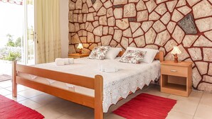 Une chambre avec un mur en pierre, un lit en bois, deux tables de chevet avec des lampes et un tapis rouge.