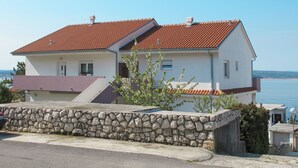 Une maison à deux étages, avec un toit recouvert de tuiles rouges, un mur de pierre à l’avant et une vue sur la mer.