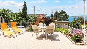 Une terrasse extérieure avec une table et des chaises, entourée de plantes et offrant une vue sur la mer.