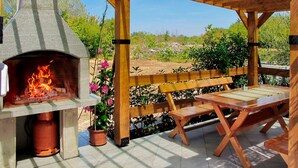 An outdoor patio with a stone-built wood-fired pizza oven, wooden benches, and a view of a natural landscape. - Andjelka by Interhome (Krk/Krk)